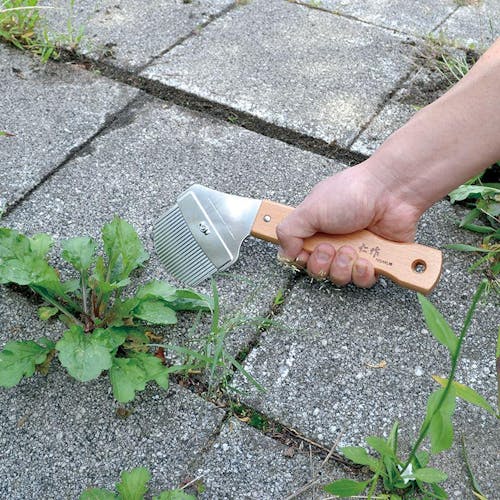 Nisaku Zassou Burush Pro S 3.25-inch Stainless Steel Weed Cutter Pro being used to remove weeds form the cracks in cement.