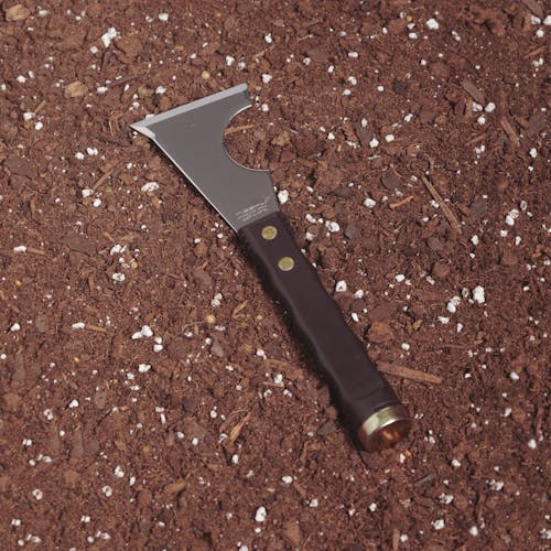 Nisaku Hamma Tsuki Kawasuki Roller Gatta 2.5-inch Japanese Stainless Steel Scraper Knife resting in soil.