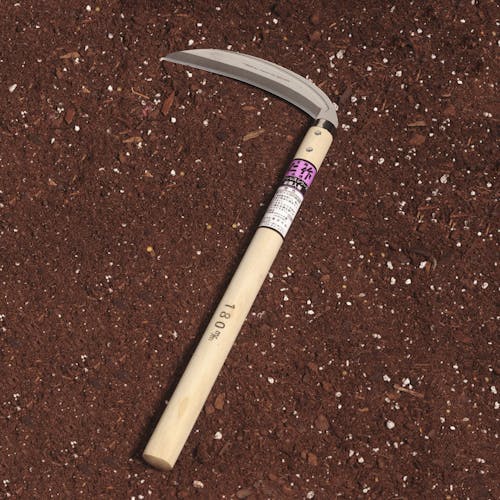 Nisaku Mikadukigama 7-inch Japanese Stainless Steel Grass Sickle laying in soil.