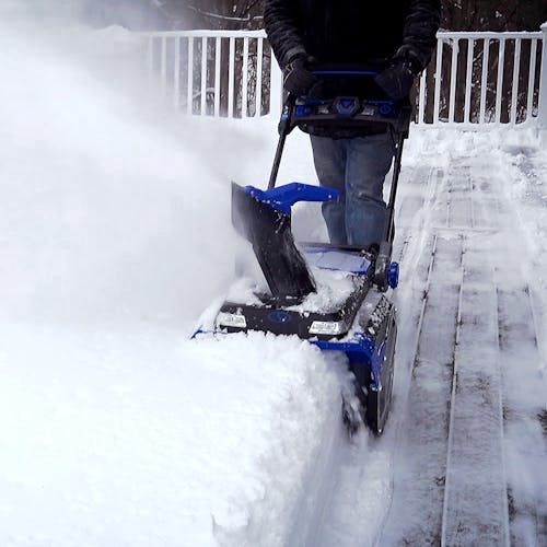 Snow Joe 100-volt 21-inch Cordless Brushless Variable Speed Single Stage Snow Blower Kit being used to clear snow off a patio deck.