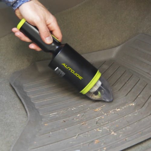 Auto Joe Cordless 8.4-Volt Handheld Vacuum Cleaner being used to clean the floor mats of a car.