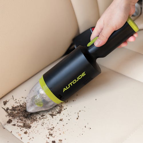 Auto Joe Cordless 8.4-Volt Handheld Vacuum Cleaner sucking up dirt from the backseat of a car.