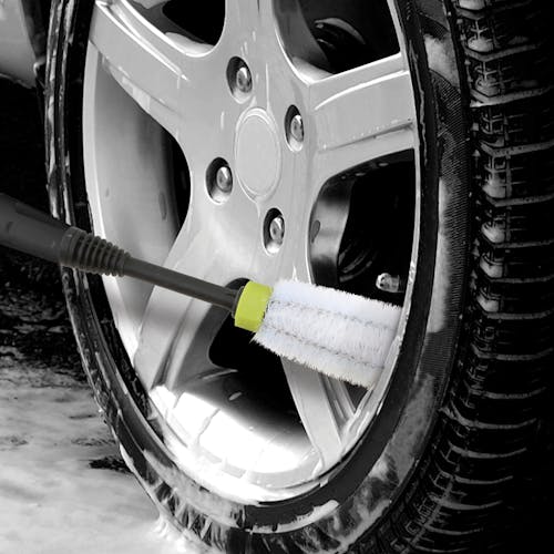 Rim and wheel brush being used to scrub clean the rims of a car.